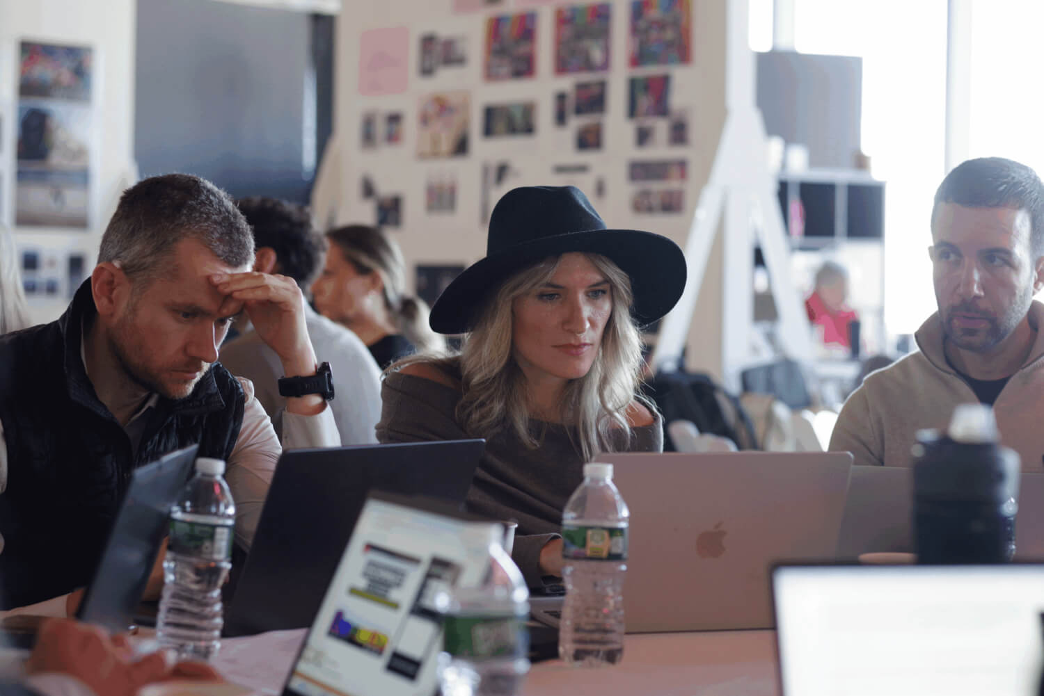 Lady wearing hat sitting at table with peers and laptops